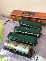 Four Lionel O-Gauge train cars displayed, including one Sunoco oil tank car and three green passenger cars, with original box for a passenger car partly visible.