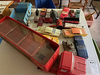 Overview of the entire collection including the large red circus truck, various metal model cars, metal tank, and blue dump truck all on a table.
