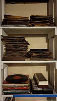 Shelved stacks of vintage vinyl records in various sleeves showing wear and aging.
