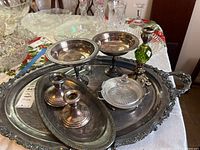 Silverplate trays, candlesticks, glass serving dish with silverplate base, and goblets arranged on a table