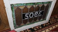 Front view of stained glass window sign showing number 3902 and surrounding colored glass panes in wood frame.