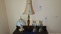 Full view of all four items on dark wood surface: two table lamps and two glass hurricane candle holders