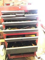 Red multi-drawer metal toolbox containing various hand tools in open drawers.