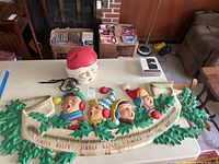 Full view of blow mold Christmas sign with four singing carolers and Santa head on table.