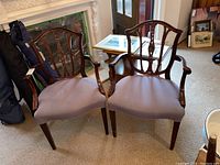 Pair of two wooden arm chairs with purple fabric upholstery shown side by side in living room environment.