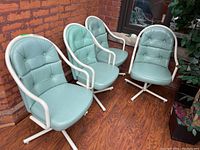 Four light blue vinyl swivel armchairs with white tubular metal frames and button-tufted tuck and roll backrests, arranged side by side against brick wall