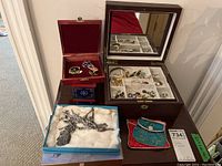 Overview of the lot showing the faux leather multi-level jewelry box open with assorted costume jewelry inside, two small wood trinket boxes, a red velvet lined box with jewelry, a blue box with a necklace on a cotton bed, and two colored pouches.