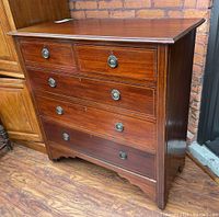 Front angled view showing the dresser's five drawers, wood finish, metal ring pulls, and shaped skirt on base.