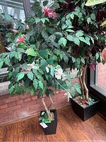 Two artificial trees; the smaller tree with green leaves and a black square planter in front, taller tree with reddish-purple and green leaves behind.