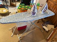 Two T-fal Ultraglide electric irons placed on one ironing board with metal frame and padded top.