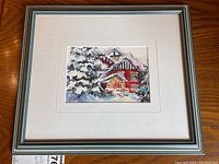 Framed watercolour painting showing winter house scene with snow-covered trees and red sled