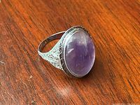 Side angled photo showing the ring's silver filigree pattern and prominent amethyst cabochon stone.