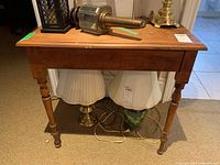 Front view of wood side table with lamps and decorative items on top, showing table's turned legs and wood grain top with cracks.