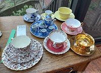 Wide view showing all teacups, saucers and the miniature tea set on a wooden surface