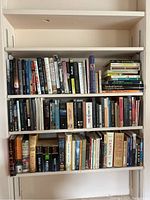 Shelf with about 50 assorted novels and non-fiction books by various well-known authors such as Wilbur Smith and James Michener.