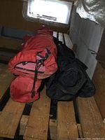 Side view of two folded camp chairs in red and black carry bags placed on wooden surface.