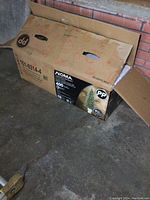 Box containing 6.5 ft Christmas tree on concrete floor, with NOMA branding visible.