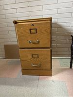 Front view of the wooden 2-drawer filing cabinet showing metal handles, lock, and overall condition.