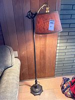 Full view of vintage floor lamp standing next to a couch showing overall height, base, pole, and lampshade.
