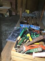 Various garden hand tools in a wooden crate with green and yellow handles and metal working ends, some rusted