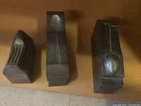 Photo showing three heavy metal casting molds on a surface, each with impressions of flatware: fork, spoon, and partial utensil.