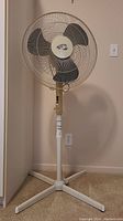Front view of the full pedestal fan showing the base, adjustable stand, and fan head with control panel.