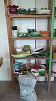 Photo of wooden shelves holding various ceramic and glass planters in assorted shapes and colors including green, orange, white, and clear glass planters, showing quantity and style variety.
