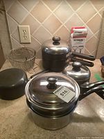 Full view of pots, steamer, double boiler, mesh baskets, and peeler on kitchen counter