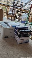 Printer body with toner cartridge boxes and stack of printer paper on carpeted floor