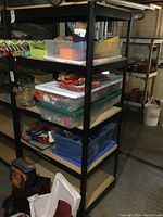 Photo showing tall black metal shelving unit loaded with various plastic storage bins and items. Shelves made of particle board with black metal frame visible.