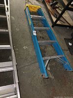 Full view of blue fiberglass ladder with aluminum rungs and yellow top step insert showing overall condition and length.