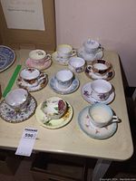 Photo showing all 10 teacups and saucers on table, various floral and patterned designs visible