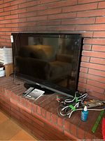 Toshiba 46 inch LCD TV sitting on brick surface, accompanied by a remote, manual, and cords.
