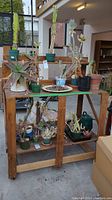 Full view of the wooden work bench with various potted plants placed on and under it to show structure and shelves.