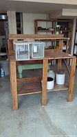 Full view of the stained wood work bench with contents on the surface and shelves; bench has a raised rear shelf and two slatted lower shelves