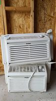 Two white Haier window air conditioners stacked, front view showing brand logo and vent grills.