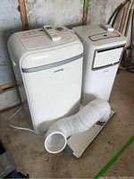 Two white KoolKing portable AC units side by side with one vent hose and remotes on top.