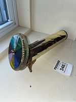 Full view of the brass kaleidoscope showing cylindrical body and colorful glass wheel end, positioned upright on the decorative tripod stand.