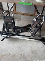 Two Malone adjustable bike racks with padded supports, rack rails, and parts laid on the floor under a table.