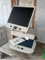 Full view of Merlin electronic video magnifier desktop unit showing LCD screen, control knobs, and manual placed on the unit.