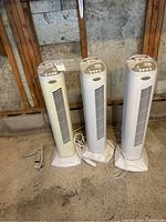 Three Forest Air tower fans standing side by side on concrete floor against wall.