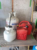 Photo of two white propane tanks and two red gasoline containers on a wooden surface in a garage.