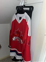 Full view of red, white, and blue Canada 1867 hockey jersey on black hanger.