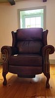 Front view of brown leather recliner with studded armrests and carved wood legs