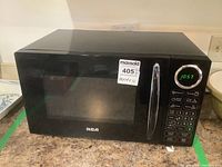 Front view of black RCA microwave oven showing door, chrome handle, and digital keypad with clock display.