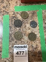 Top view of five coins on a speckled brown countertop with green masking tape border and auction tag seen at bottom