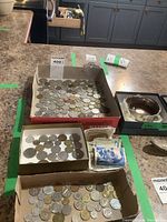 Wide view of the coin collections and banknotes in three cardboard trays on a kitchen counter, showing the quantity and variety of coins along with some packaging in the background.