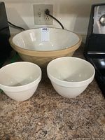 Three ceramic bowls on kitchen counter: large beige TG Green mixing bowl with white interior, two smaller white steamed pudding pots in front.