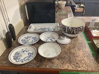 Overview of six porcelain items and one covered metal bowl on a kitchen counter.