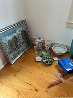 Photo shows original signed oil painting on canvas, decorative ceramic and pottery items including bowl, jar with lid, pitcher, small plates, goblet, and a hand-painted terracotta box arranged on wooden floor.